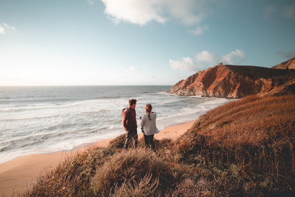 man and woman standing on brown grass field near ocean