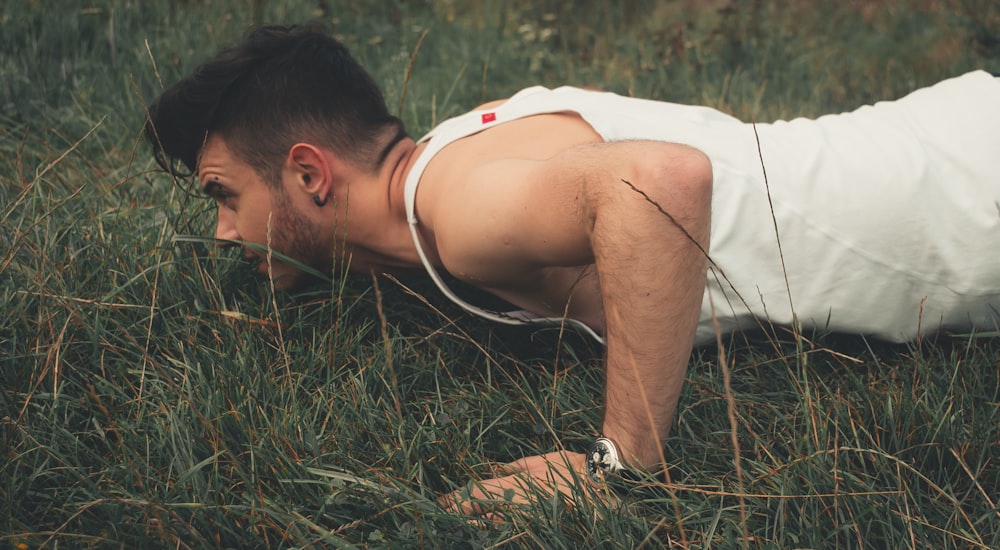 man wearing white tank top pruning on green grass