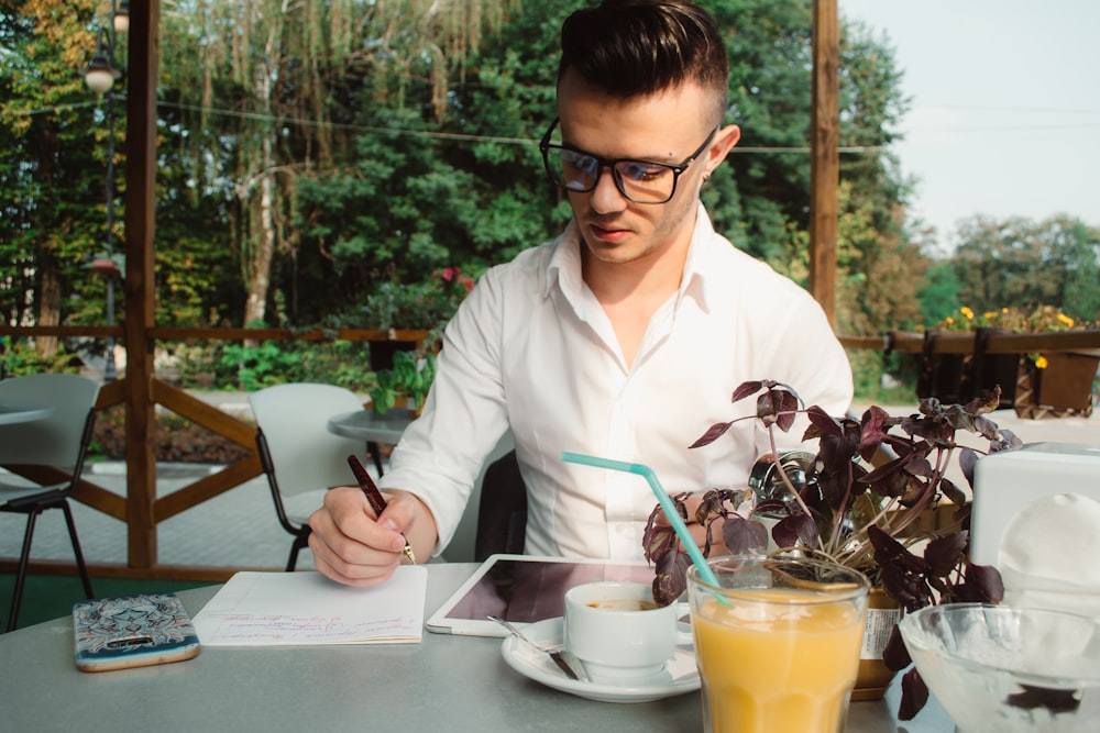 man wearing white dress shirt writing on white paper