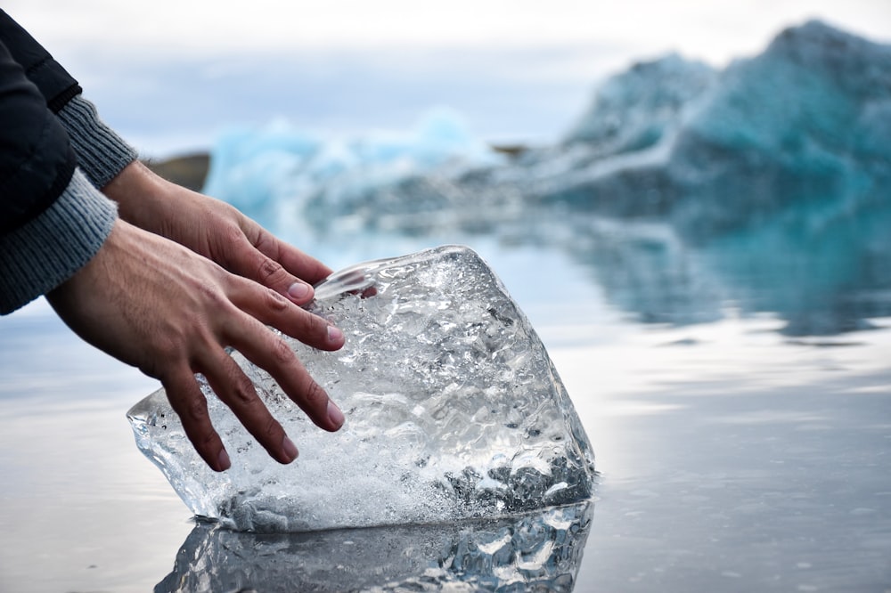 person with hands on ice block on water during daytime