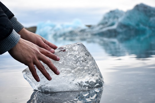 person with hands on ice block on water during daytime in Jokulsarlon Iceland