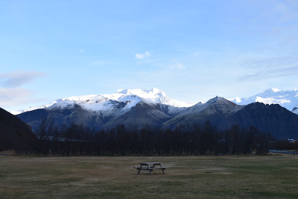 雪をかぶった山々を見下ろす草原の真ん中にある木製のピクニックテーブル