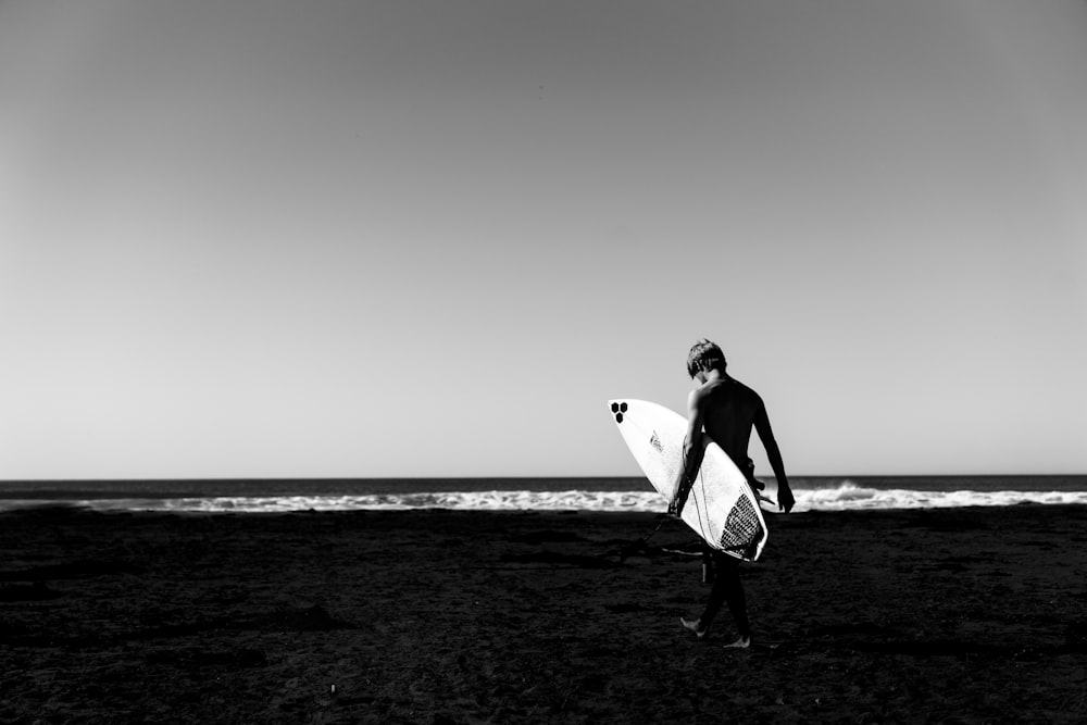 fotografia in scala di grigi dell'uomo che tiene la tavola da surf