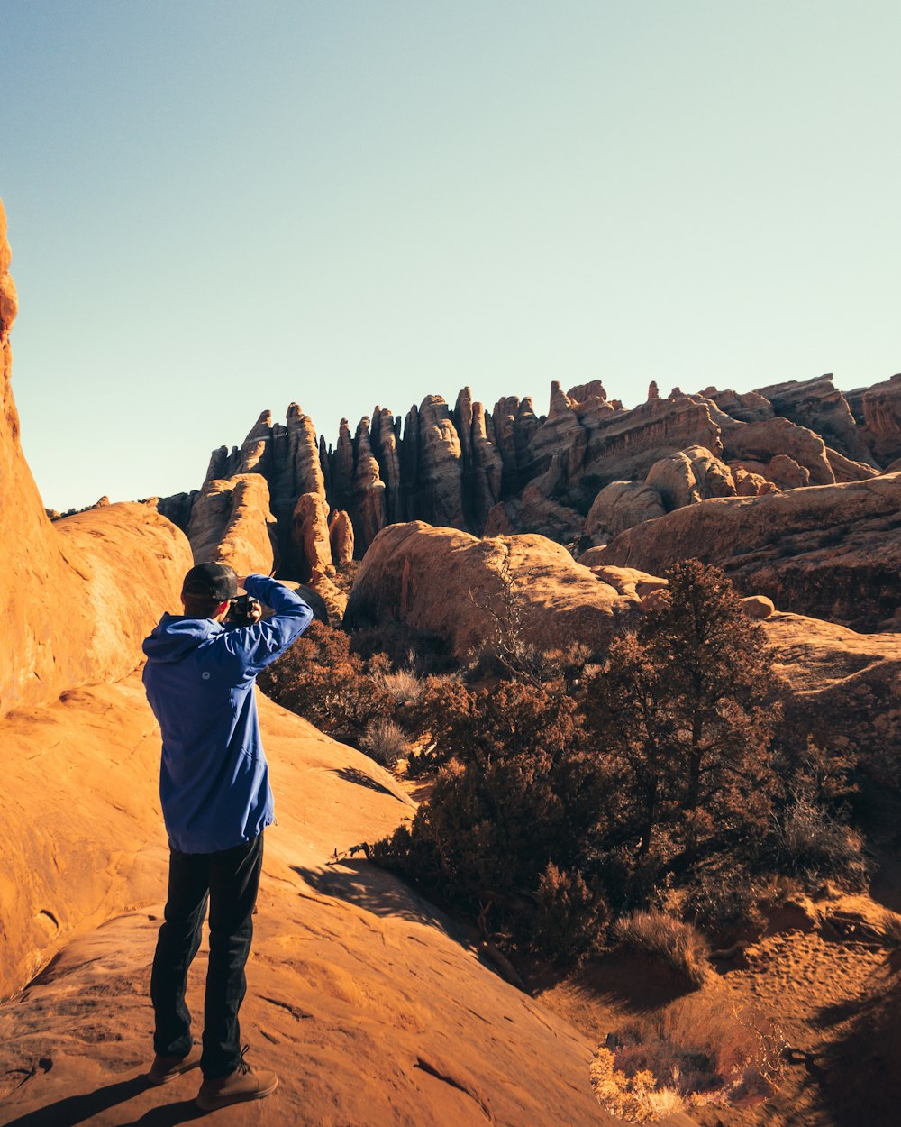 hombre en sudadera con capucha azul tomando fotos de la formación rocosa