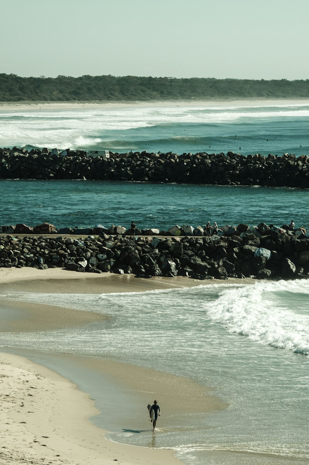 man walking along seashore carrying surfboard