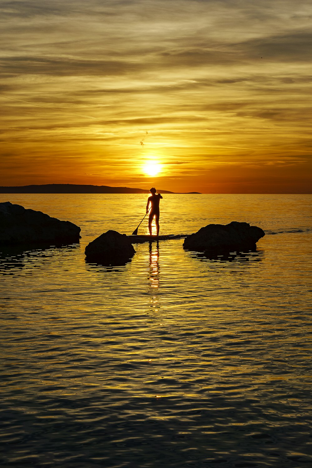 silhouette photography of man standing on paddleboard floating in ocean