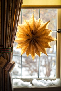 A snowy window scene with hanging star-shaped lights casting a warm glow inside.