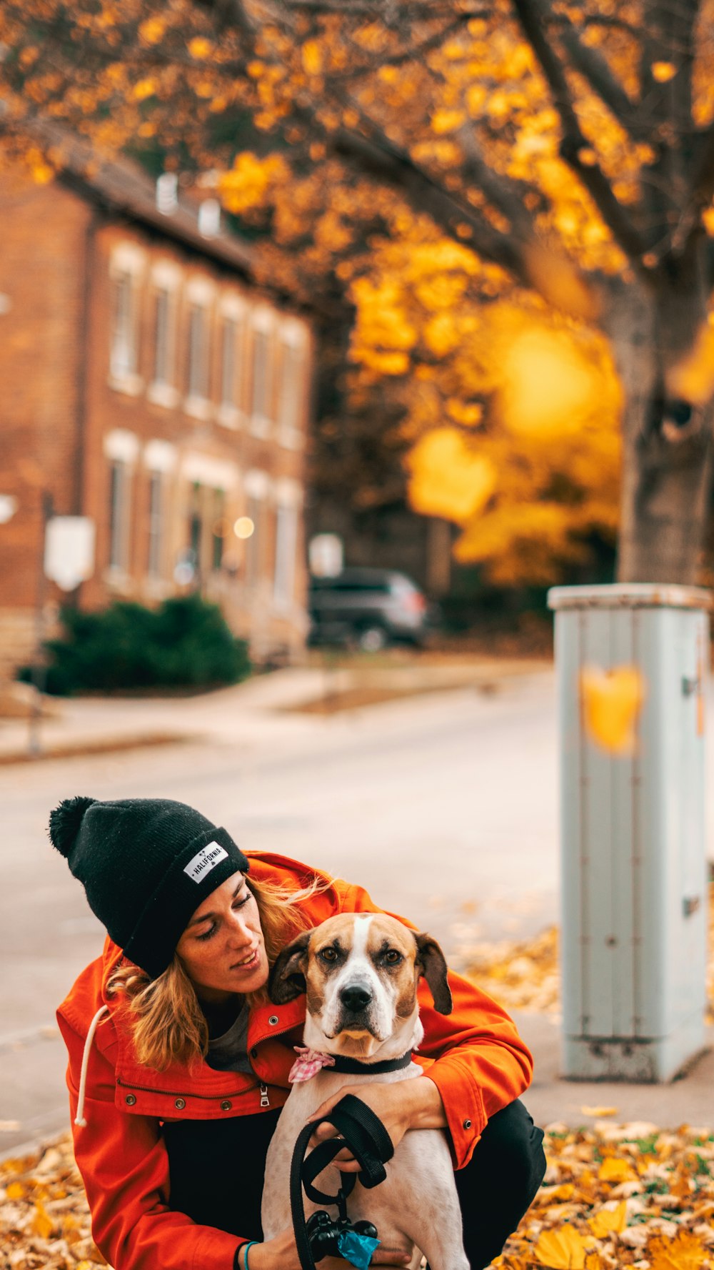 Frau mit orangefarbener Jacke, die braunen Hund umarmt