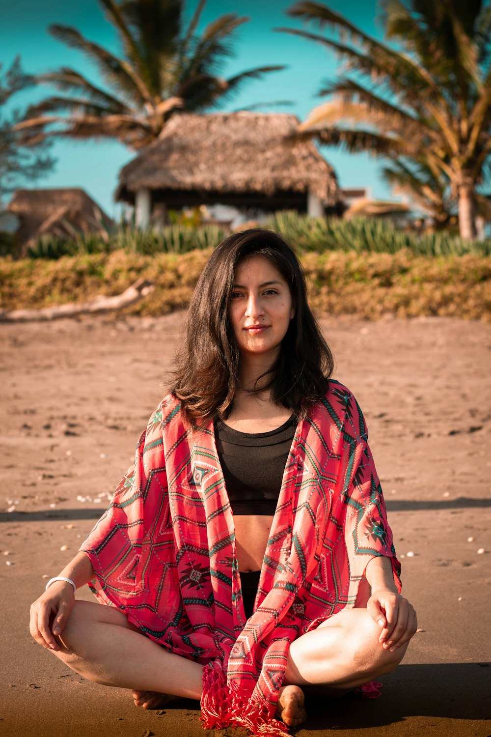 woman wearing black crop top and black shorts Indian sitting on beach sand during daytime