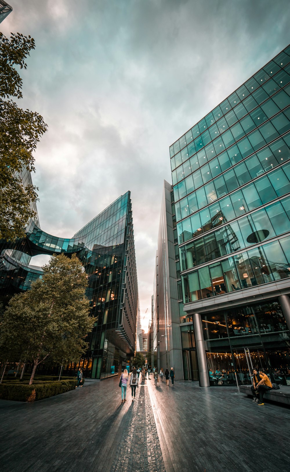 people walking between curtain wall buildings under cloudy sky during daytime