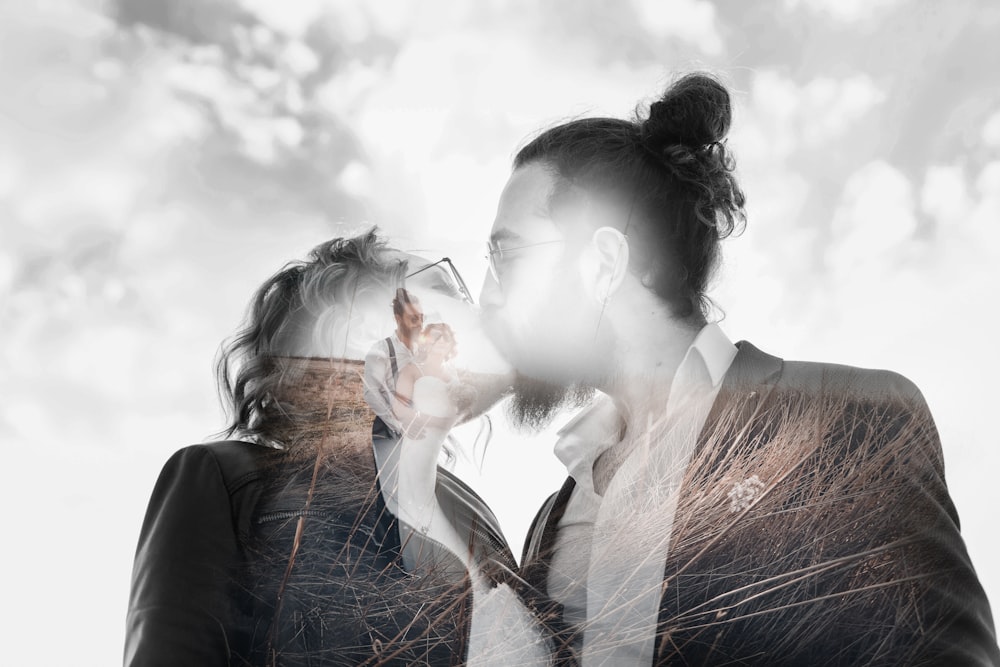 grayscale photo of man and woman kissing under cloudy sky