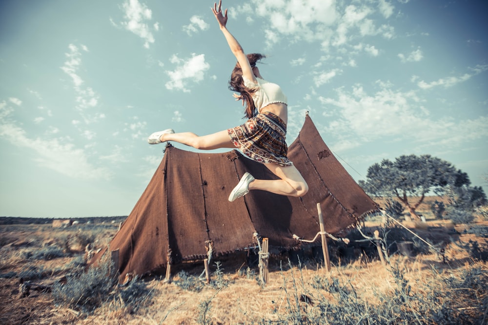 jumping woman near brown tent on field during daytime