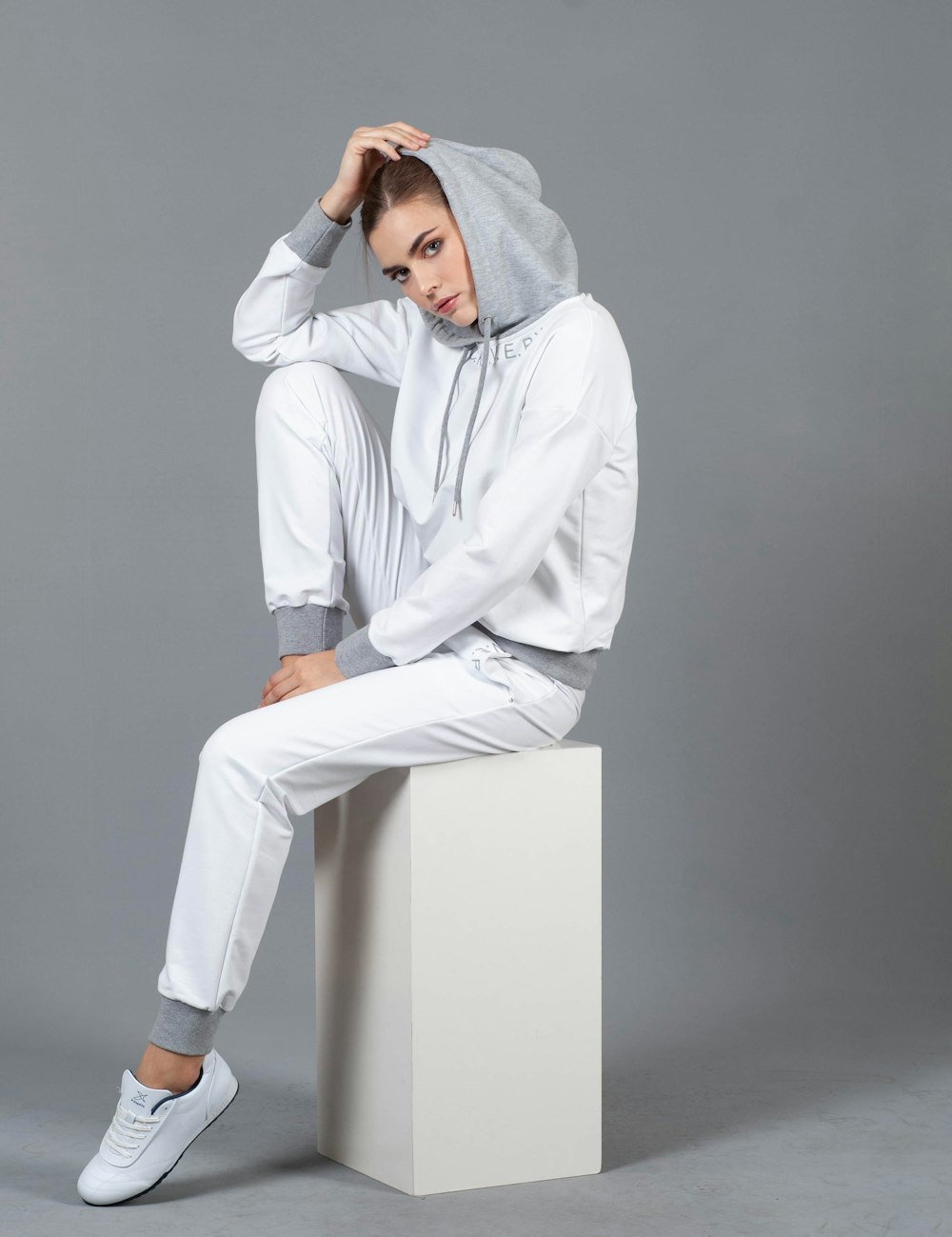 woman sitting on white box wearing hoodie holding her head