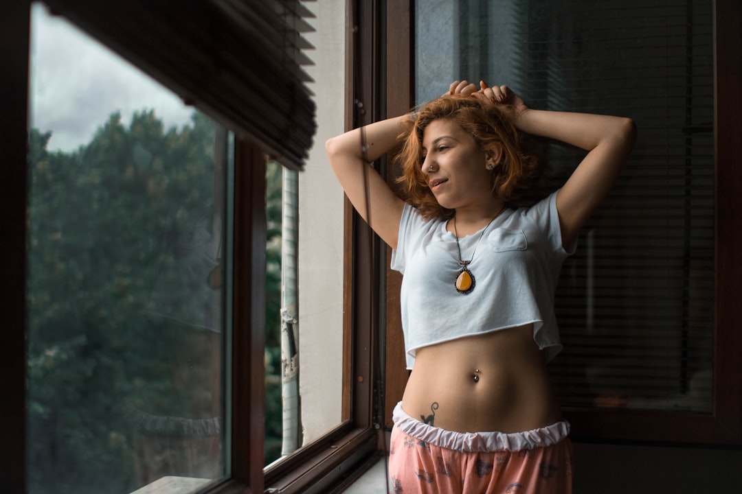 woman wearing gray crew-neck crop-top and pink pajama pants near window during daytime