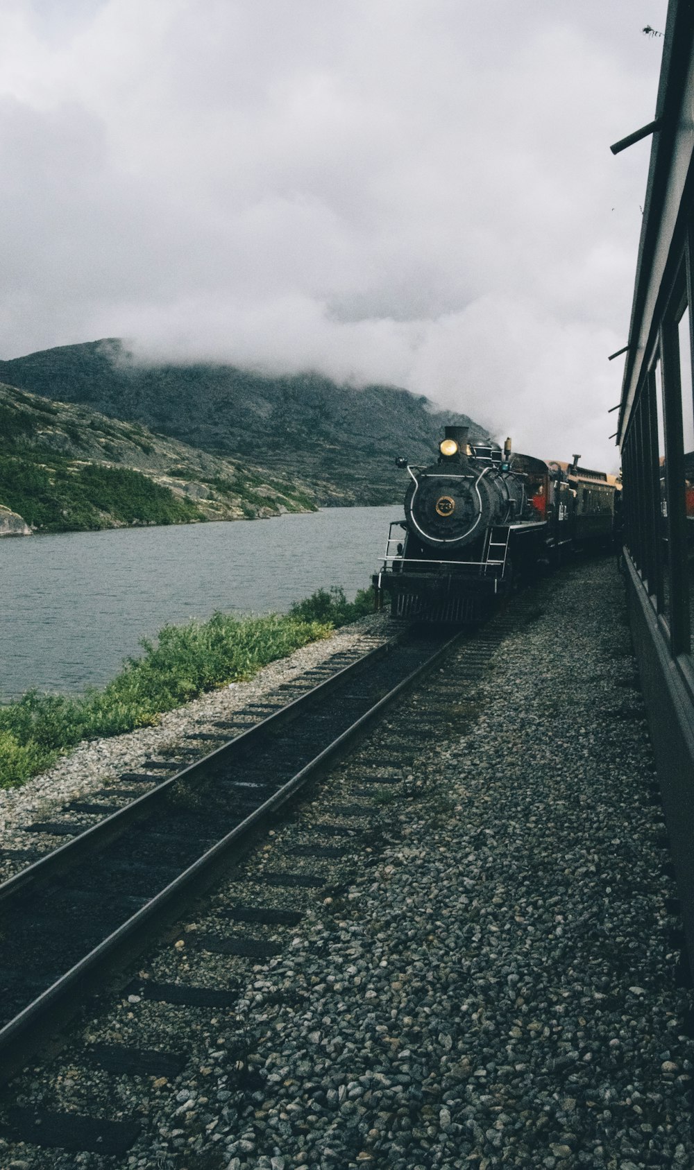 昼間、曇り空の下、水辺を通り過ぎる黒い列車