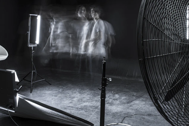 A moody, gun metal grey-toned studio scene with AI-generated art on screens and film equipment subtly lit in the background.