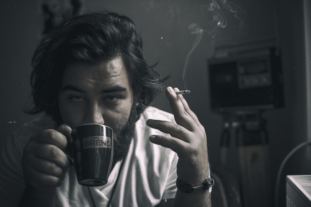 man holding cigarette while drinking cup