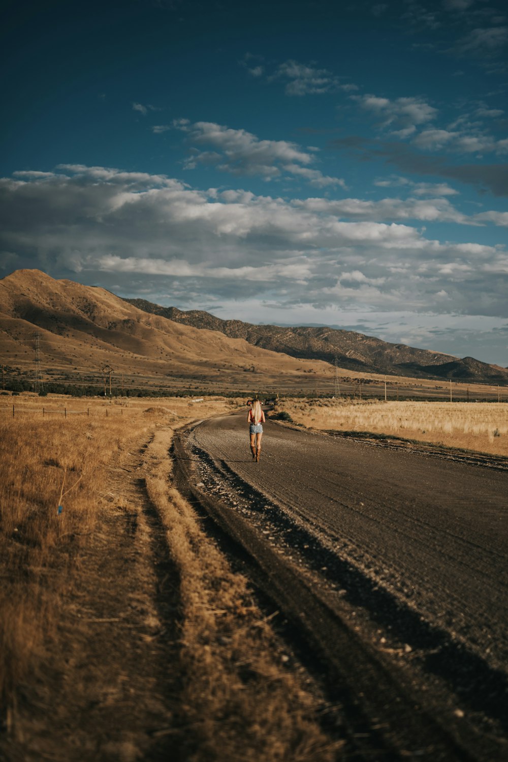 woman walking on road beside field overlooking mountains at daytime