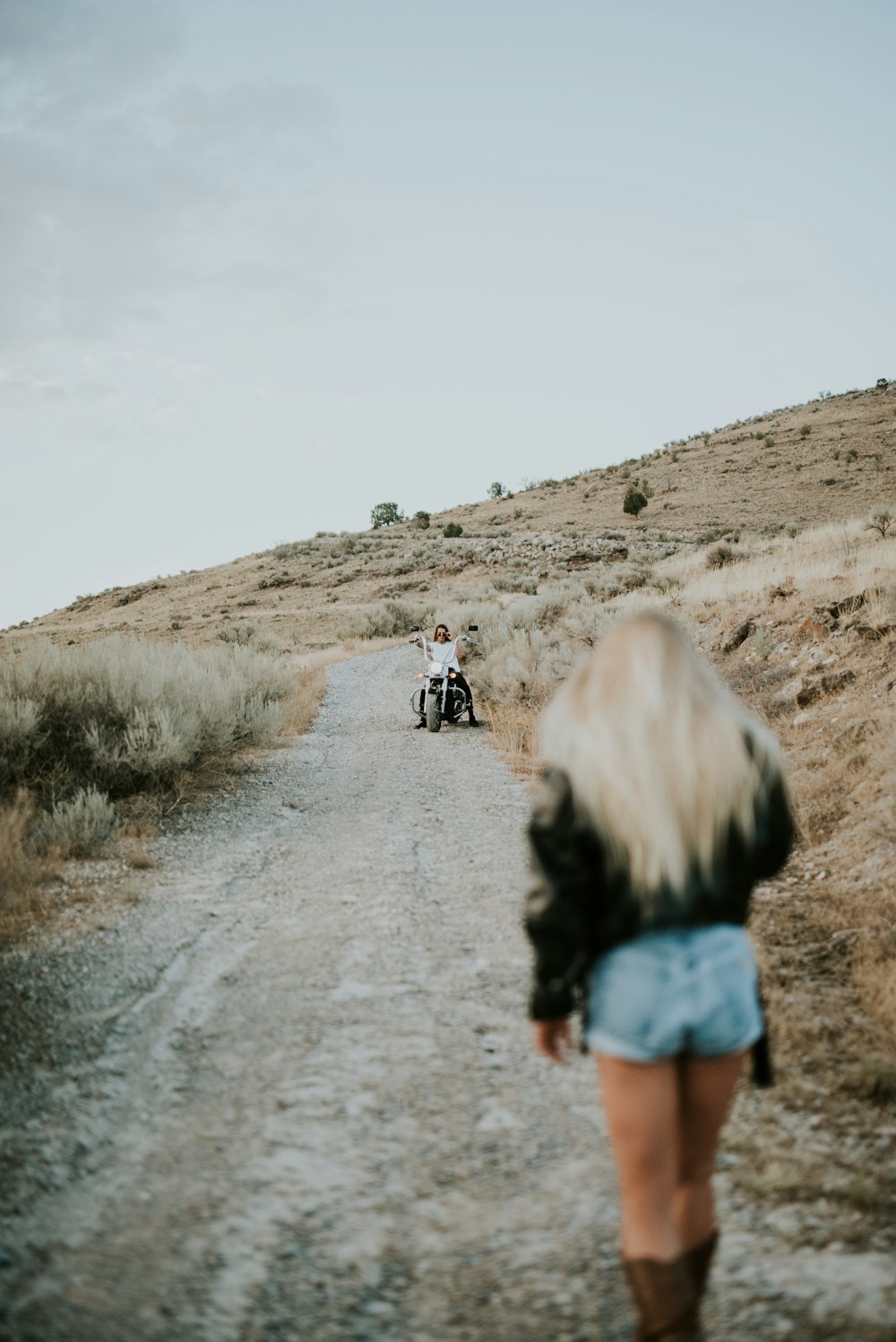 woman in black jacket heading to person riding chopper motorcycle on rough road