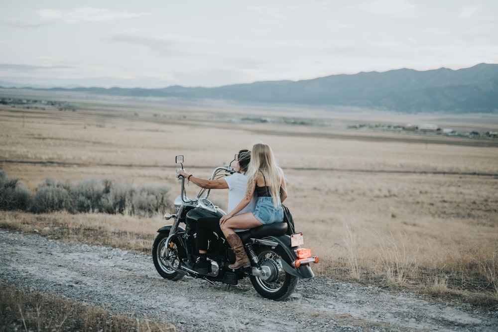Homem e mulher andando em motocicleta cruiser passando na estrada ao lado do campo durante o dia