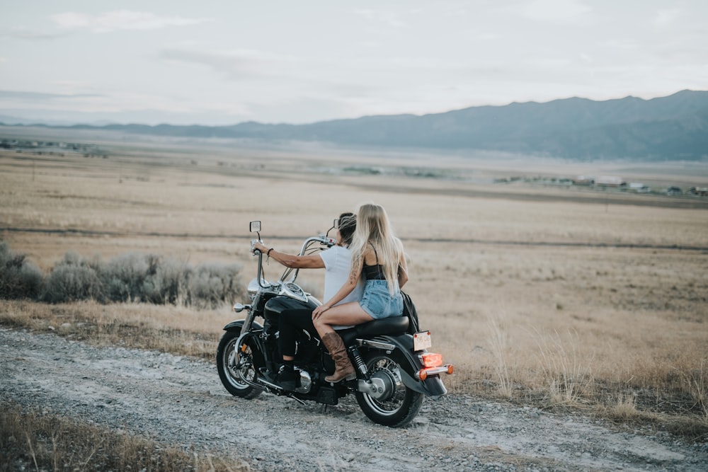 man and woman riding on cruiser motorcycle passing on road beside field at daytime