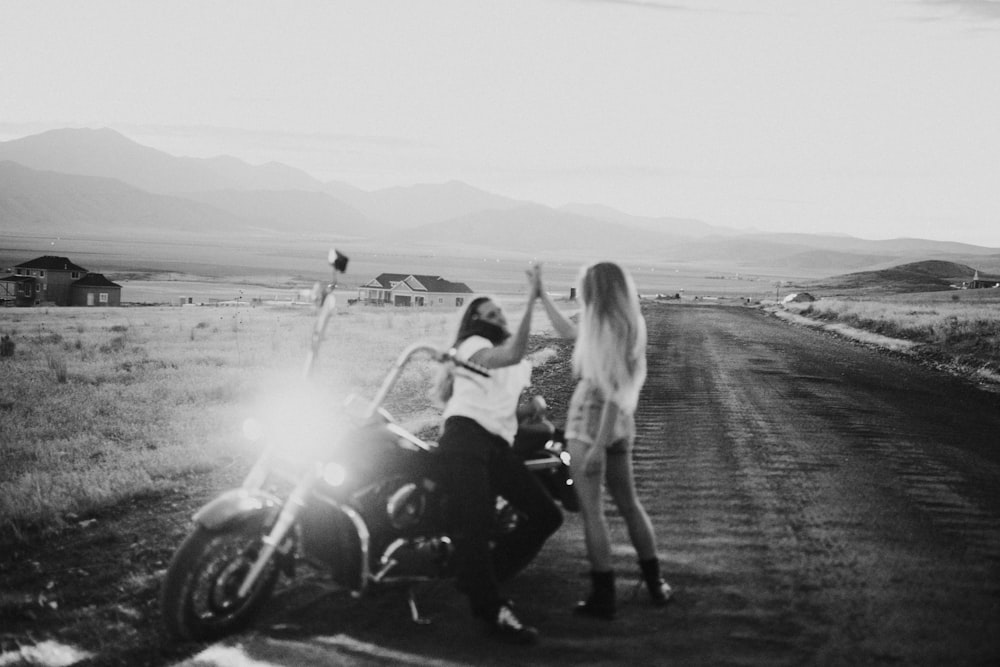 foto em tons de cinza de duas mulheres perto da motocicleta cruiser