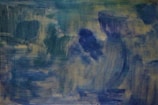 An abstract composition featuring a blend of muted greens, blues, and purples. The brushstrokes create a sense of movement, with various shades overlapping in a loose, layered pattern. The overall texture is soft and painterly, evoking a dreamy, introspective atmosphere.