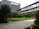 A modern building with multiple floors featuring large windows and a sleek design. There is a landscaped courtyard with well-maintained grass, palm trees, and other greenery. The architecture includes a mix of glass and wood elements, with outdoor balconies on some of the levels.