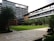 A modern building with multiple floors featuring large windows and a sleek design. There is a landscaped courtyard with well-maintained grass, palm trees, and other greenery. The architecture includes a mix of glass and wood elements, with outdoor balconies on some of the levels.