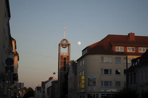 A city street at dusk, with shops and apartment buildings under the moon
