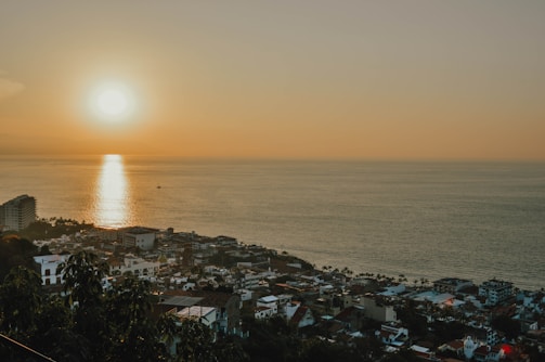 Coastal city skyline at sunset with buildings and sea.
