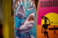 Two surfboards are depicted, one with an illustration of sharks, featuring a large shark with an open mouth and other smaller sharks around it. The other surfboard has a vibrant design with a silhouette of a surfer against a yellow and pink sunset background.
