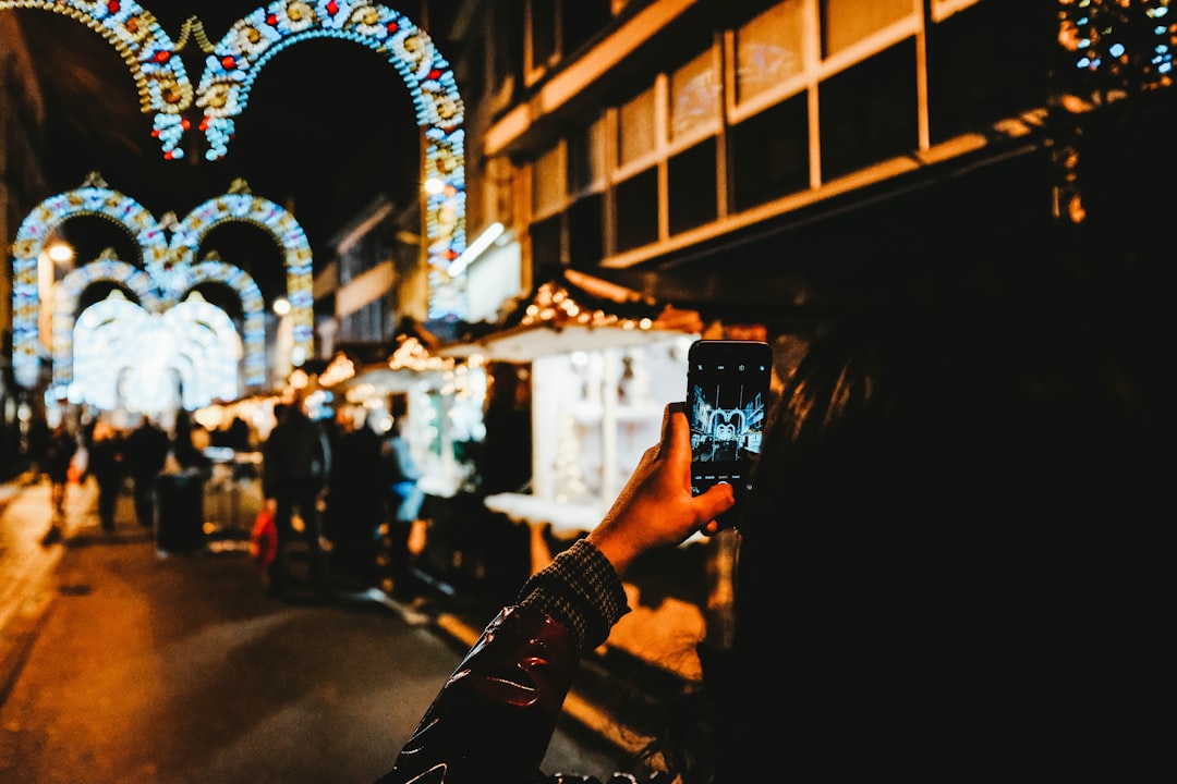 woman taking photo of people standing between buildings at night