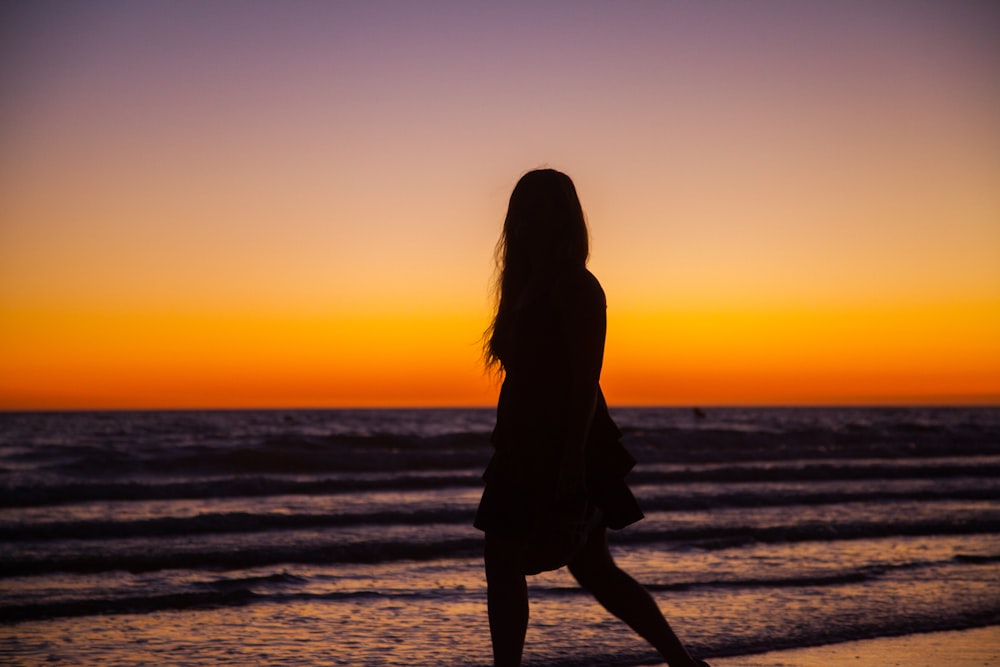 silhouette photography of woman walking on seashore