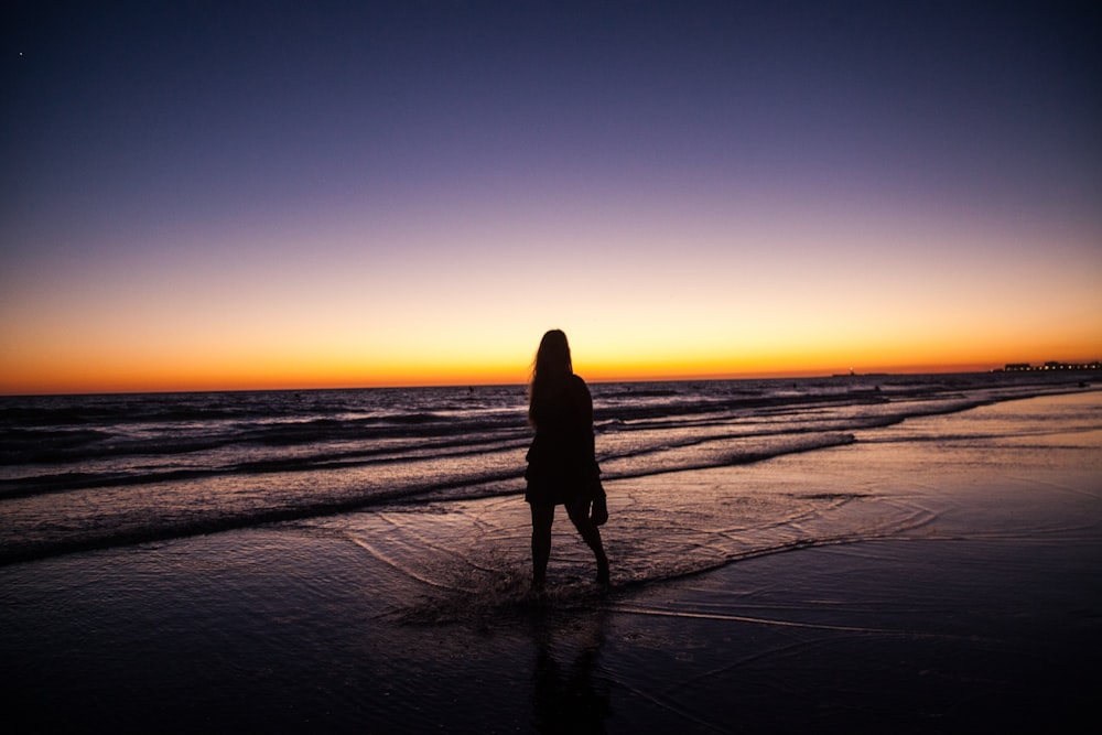 석양 아래 바닷가에 서 있는 여자
