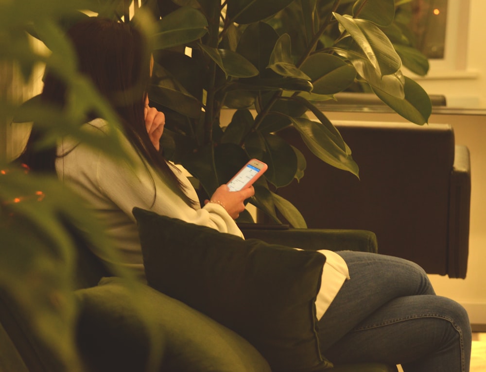 person using smartphone while sitting on black sofa between green plants
