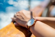A wrist wearing a luxury watch, holding a cold drink with a beach sunset in the background.