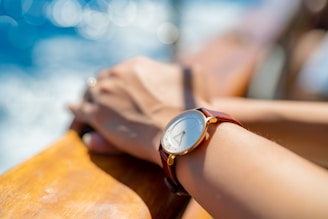 A wrist wearing a luxury watch, holding a cold drink with a beach sunset in the background.