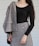 A person is wearing a black long-sleeve top paired with a gray, textured skirt and draped fabric over one shoulder. The outfit features decorative buttons, and the overall pattern has a tweed-like appearance. The setting is plain with a light-colored background.