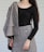 A person is wearing a black long-sleeve top paired with a gray, textured skirt and draped fabric over one shoulder. The outfit features decorative buttons, and the overall pattern has a tweed-like appearance. The setting is plain with a light-colored background.