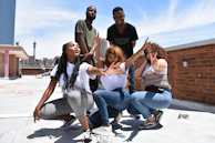 Wide shot of a group of men in terravibe outfits gathered on an urban rooftop, city lights glowing behind them.