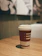 Close-up of elegant disposable coffee cups on a wooden café table with soft natural light.
