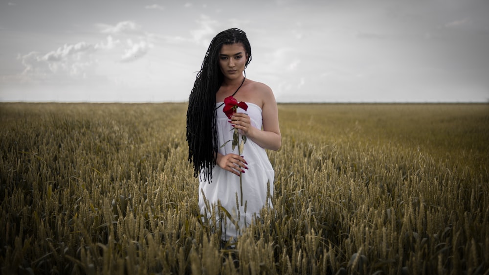 woman wearing white dress holding rose standing on the grass field