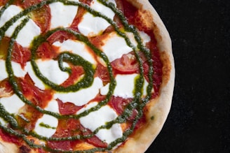 A vibrant close-up of a semi-sourdough crust pizza topped with pesto-ranch sauce, fresh basil, and melted cheese.