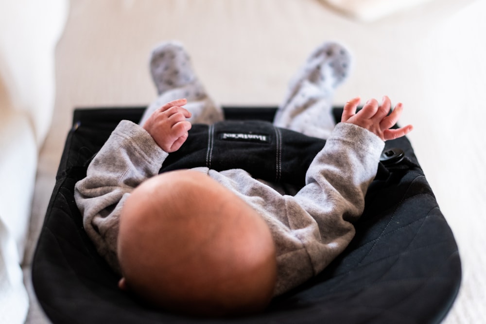 baby wearing gray onesie on black bouncer