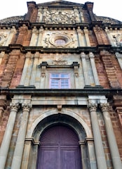 A historical facade of a grand building featuring intricate architectural details such as ornate carvings, columns, and arched windows. The structure is predominantly made of stone with decorative elements highlighting its heritage.