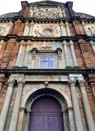 A historical facade of a grand building featuring intricate architectural details such as ornate carvings, columns, and arched windows. The structure is predominantly made of stone with decorative elements highlighting its heritage.