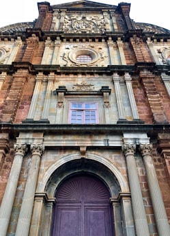 A historical facade of a grand building featuring intricate architectural details such as ornate carvings, columns, and arched windows. The structure is predominantly made of stone with decorative elements highlighting its heritage.