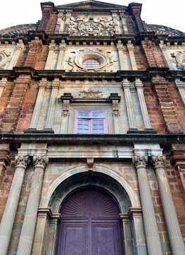 A historical facade of a grand building featuring intricate architectural details such as ornate carvings, columns, and arched windows. The structure is predominantly made of stone with decorative elements highlighting its heritage.