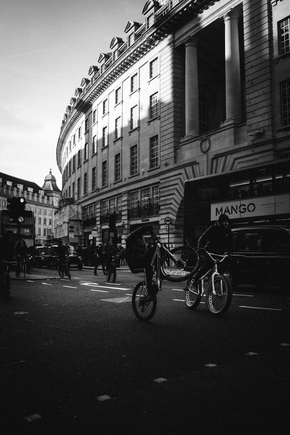 greyscale photo of crowd and riding bicycle near building